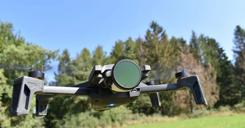 Drone noir avec caméra, planant au-dessus d'un paysage verdoyant